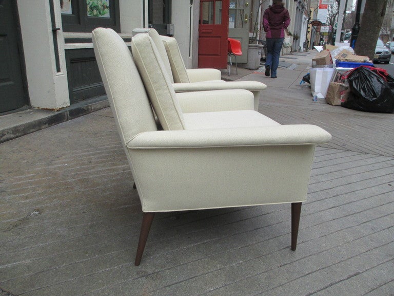 Pair of cream colored tailored arm chairs on wooden spike legs with removable cushions and trapezoidal arms  